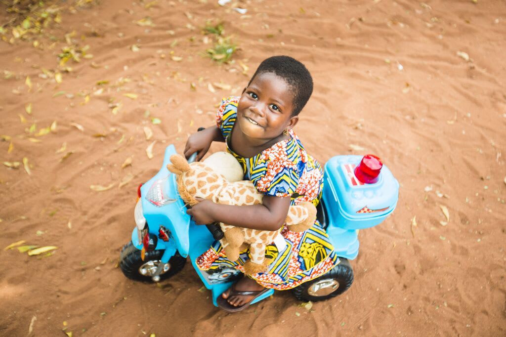 Little girl holding giraffe stuffy is on a blue tricycle